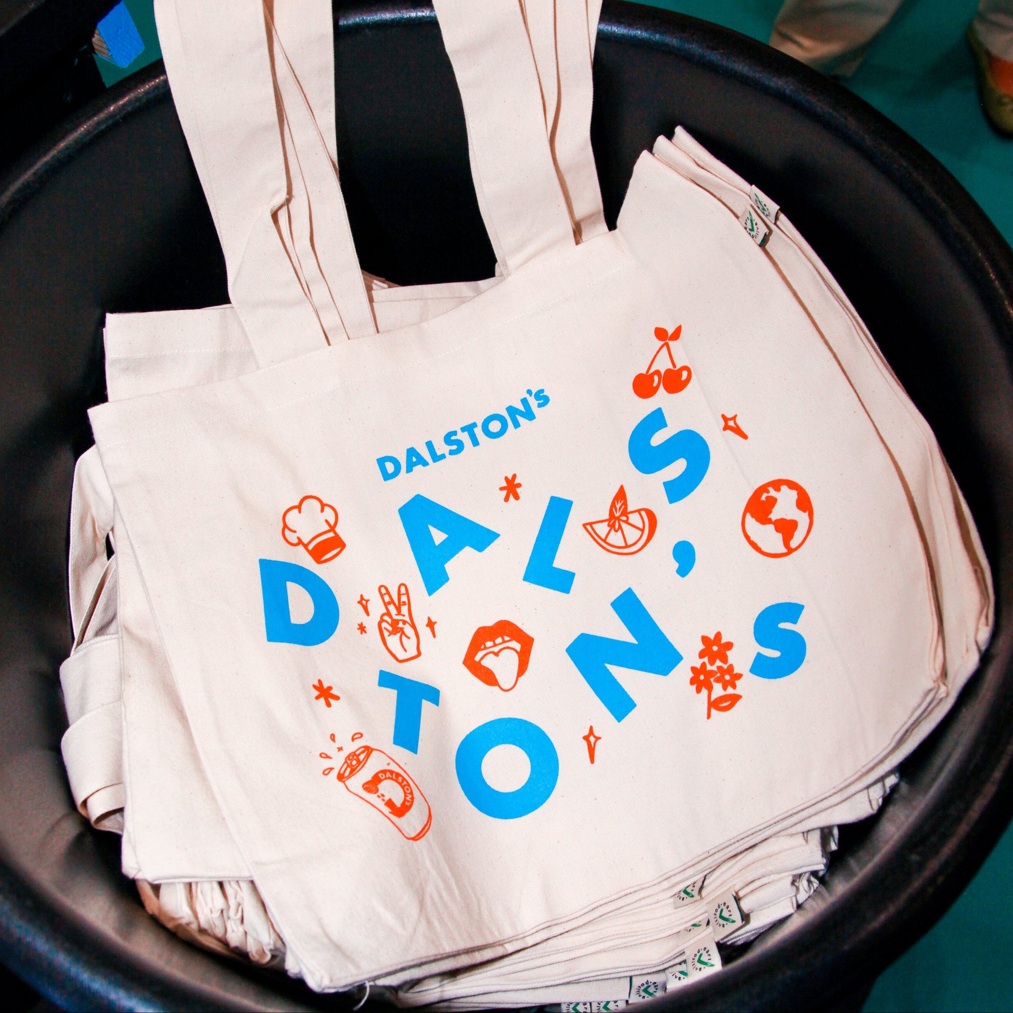 Stack of white tote bags with colorful text and graphics.